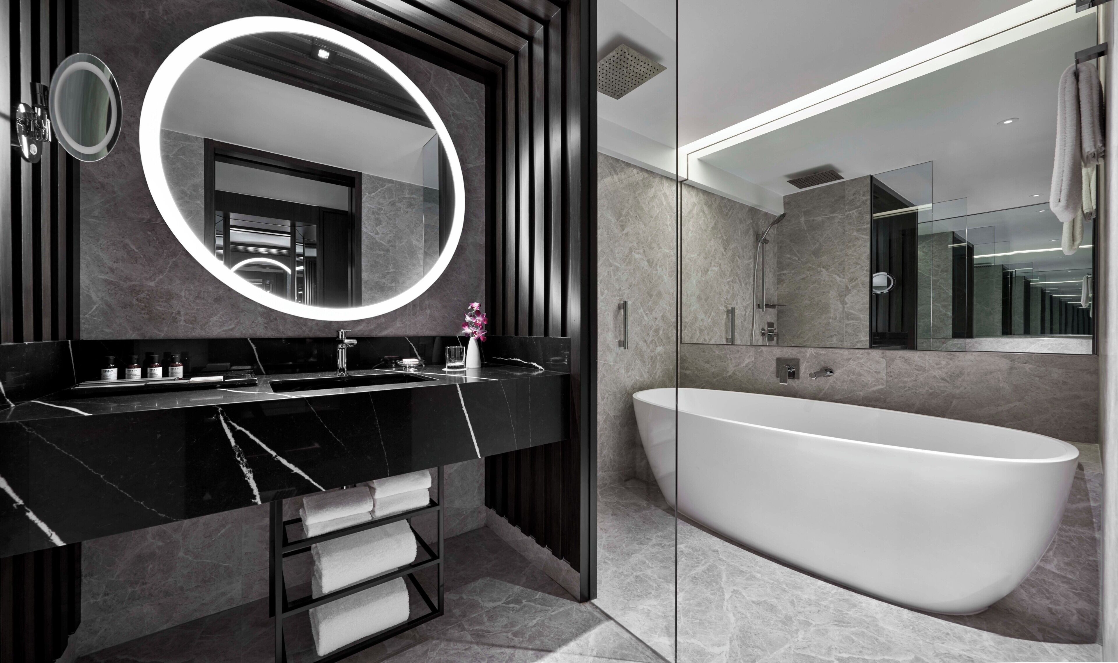 A modern bathroom with a freestanding bathtub, a round mirror with a light, and a dark-toned vanity.