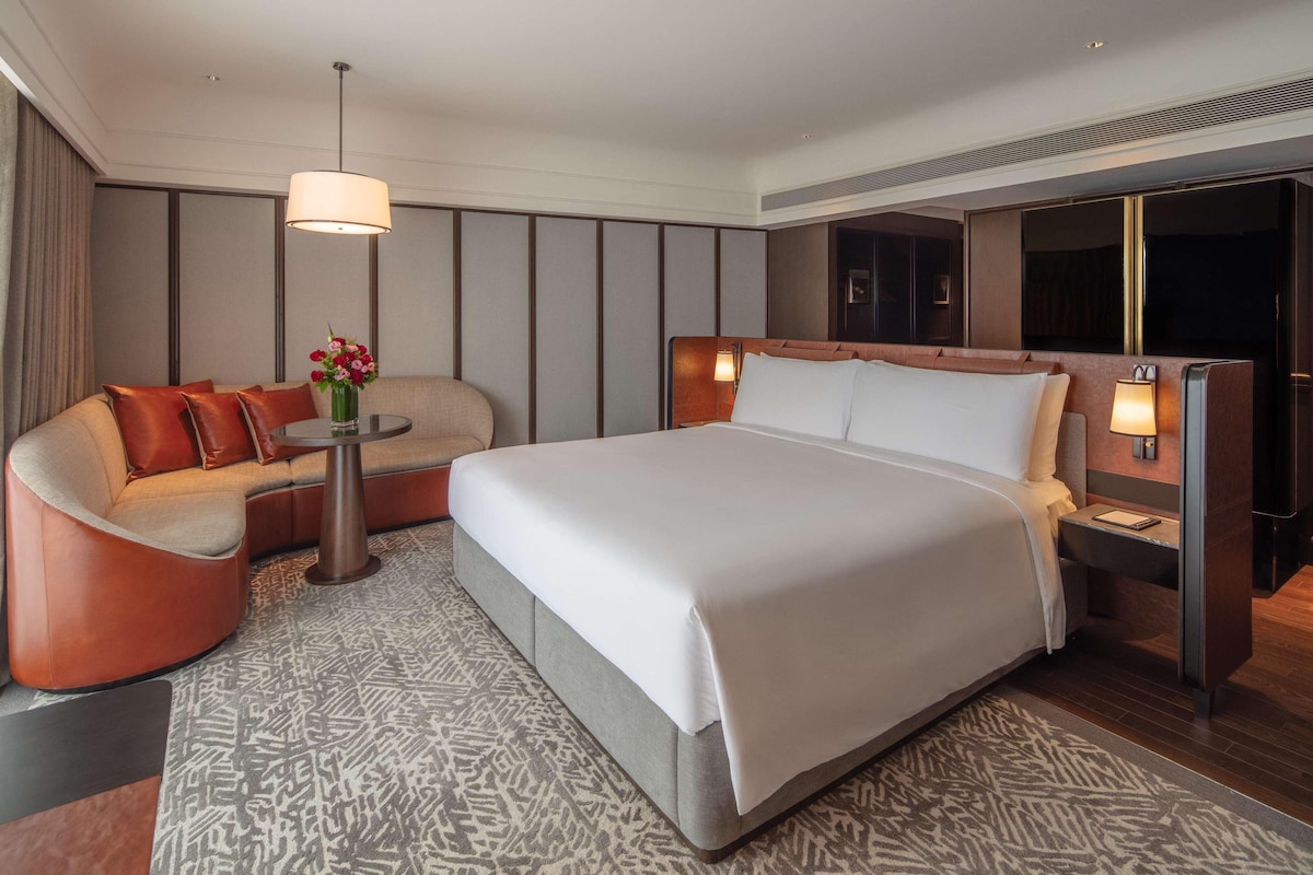 Une chambre d’hôtel moderne avec un grand lit, un canapé, une petite table agrémentée de fleurs et une table de chevet avec une lampe.