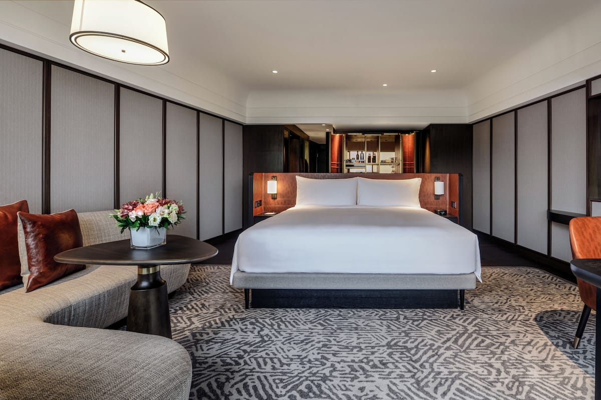 Een hotelkamer met een groot bed, een bank, een kleine tafel met een bloemenvaas, een televisie en een bureau met een stoel.