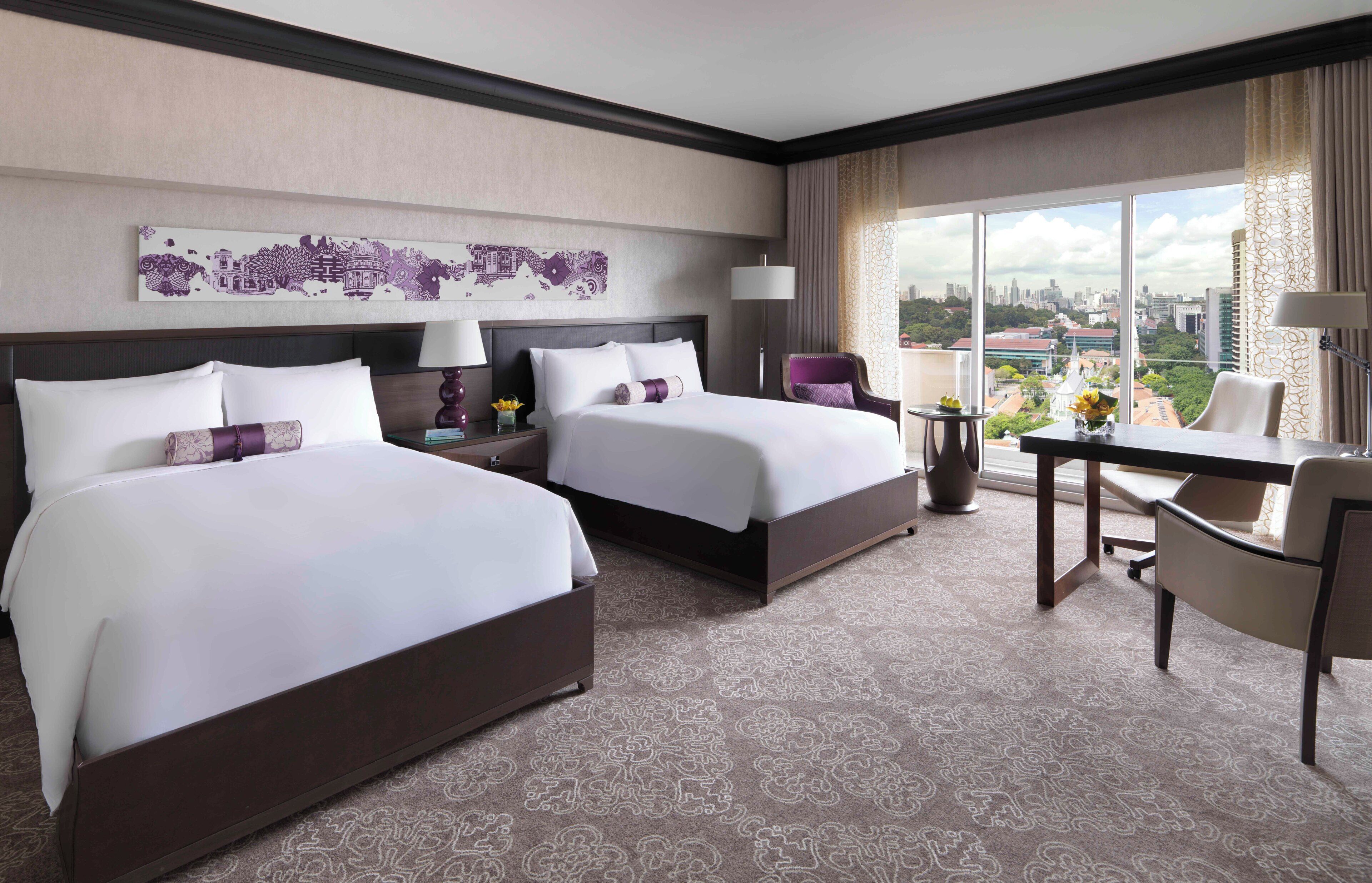 A hotel room with two beds, a desk, a chair, a city view, and a decorative wall piece.