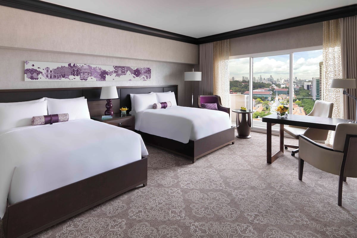 A hotel room with two beds, a desk, a chair, a city view, and a decorative wall piece.