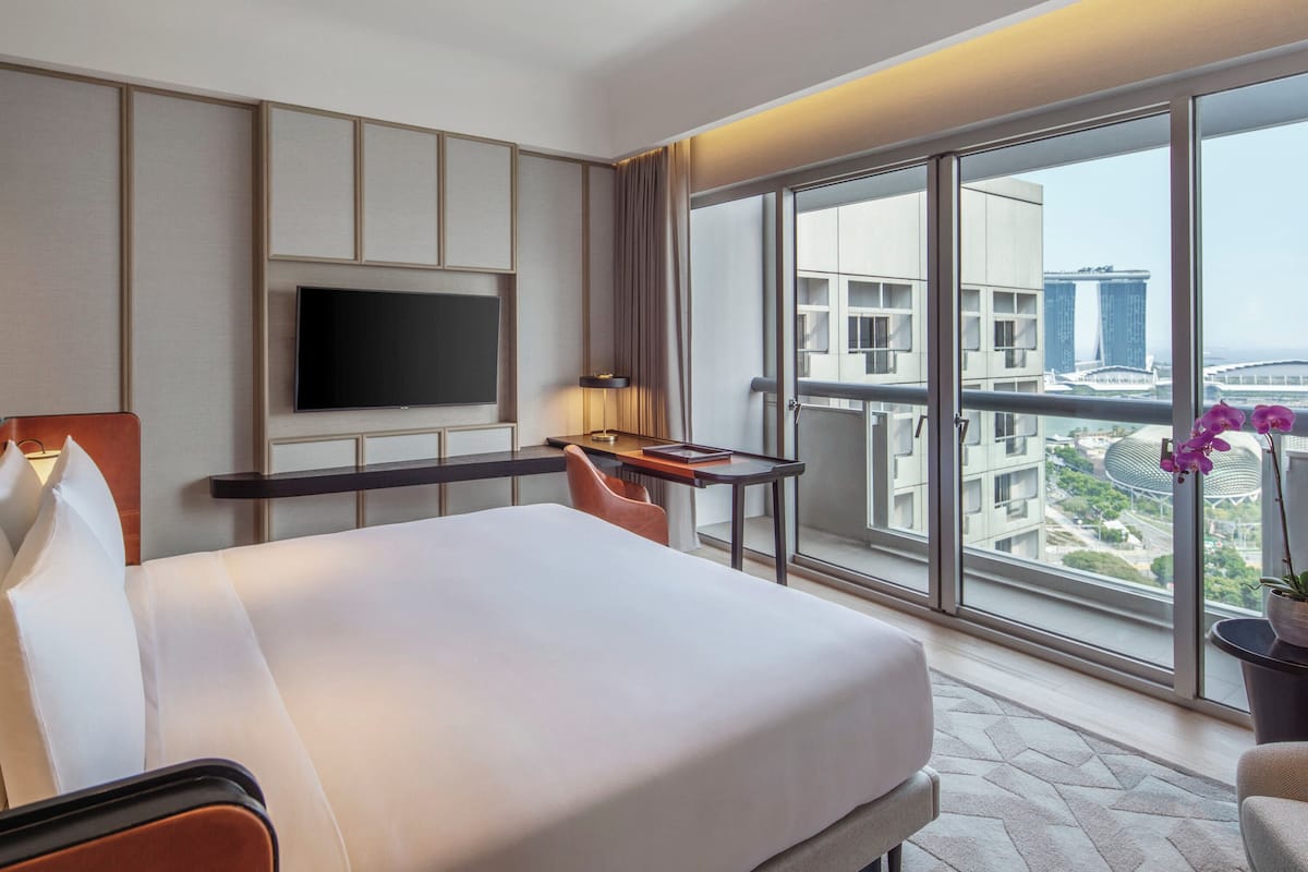 Een hotelkamer met een bed, een televisie, een bureau en een groot raam met uitzicht op de stad.