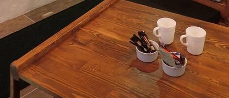 A wooden table with two white mugs and a cup of coffee, a plaid bench, and a television mounted on the wall.