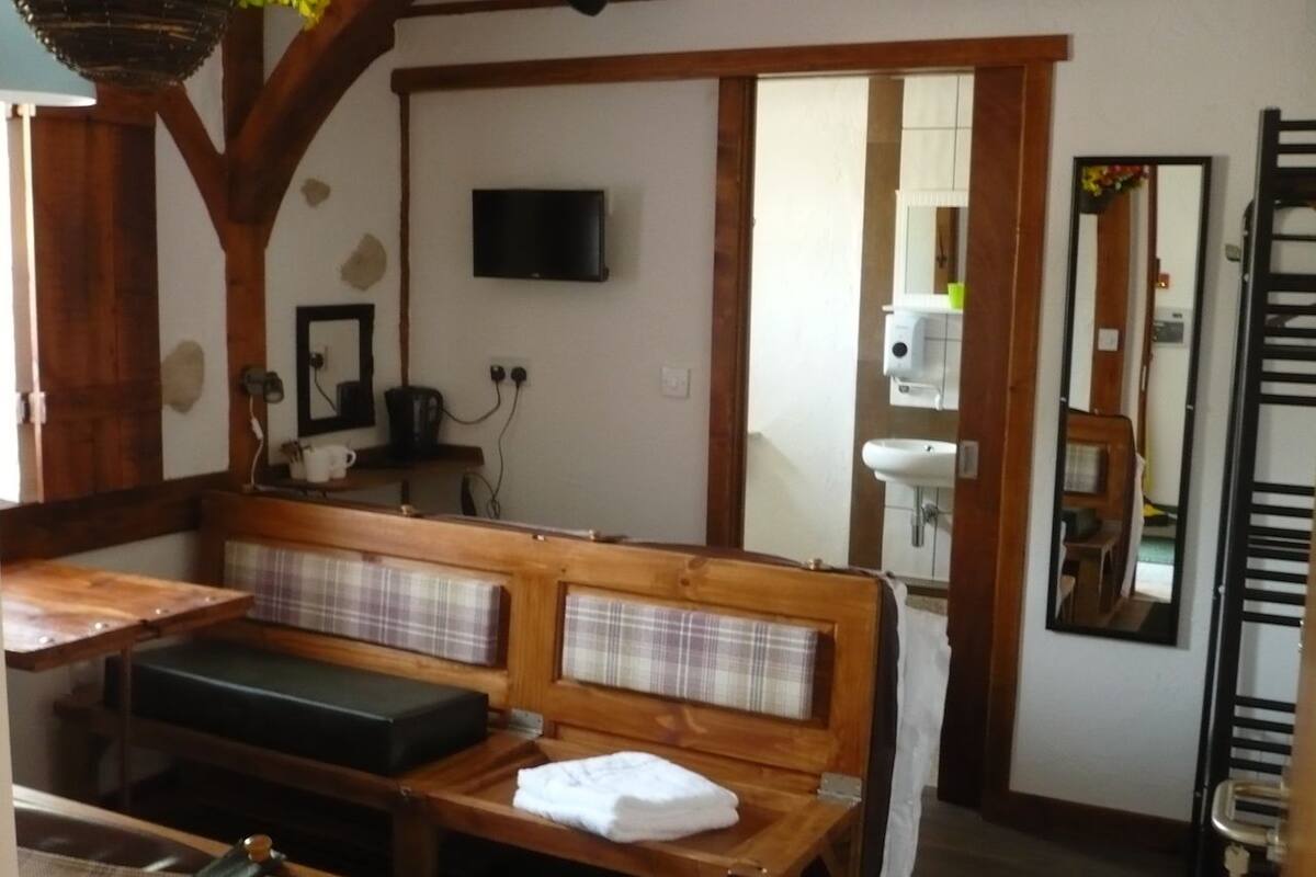 Une pièce chaleureuse avec un banc en bois, une petite table, un téléviseur et un miroir.
