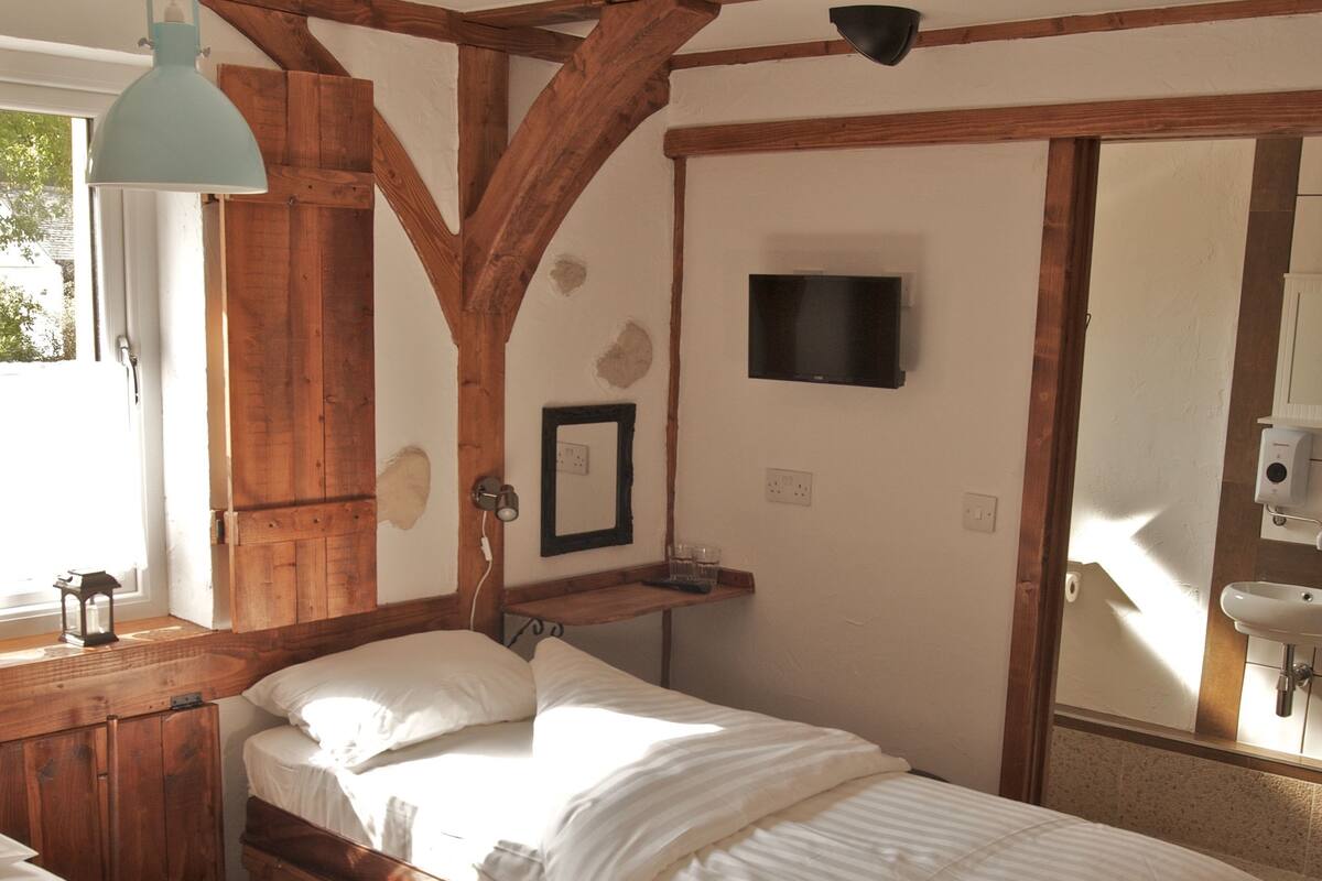 Une chambre avec deux lits, des poutres en bois, une télévision, un miroir et une fenêtre.