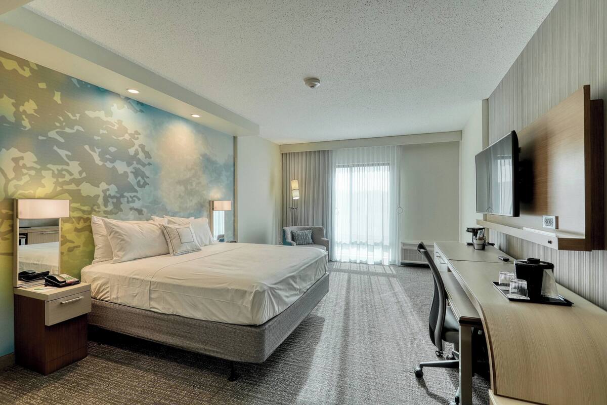 A hotel room with a large bed, a desk, a television, and a window with curtains.