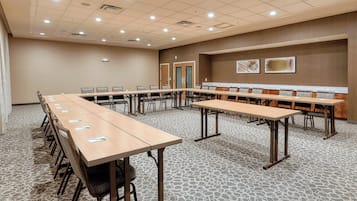 A conference room with long tables and chairs, a patterned carpet, and a wooden wall with two framed pictures.