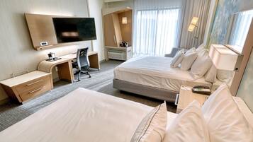 Une chambre d’hôtel avec deux lits, un bureau, une télévision et une grande fenêtre avec des rideaux.