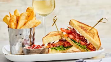 A sandwich cut in half with a side of fries and a glass of white wine on a plate.