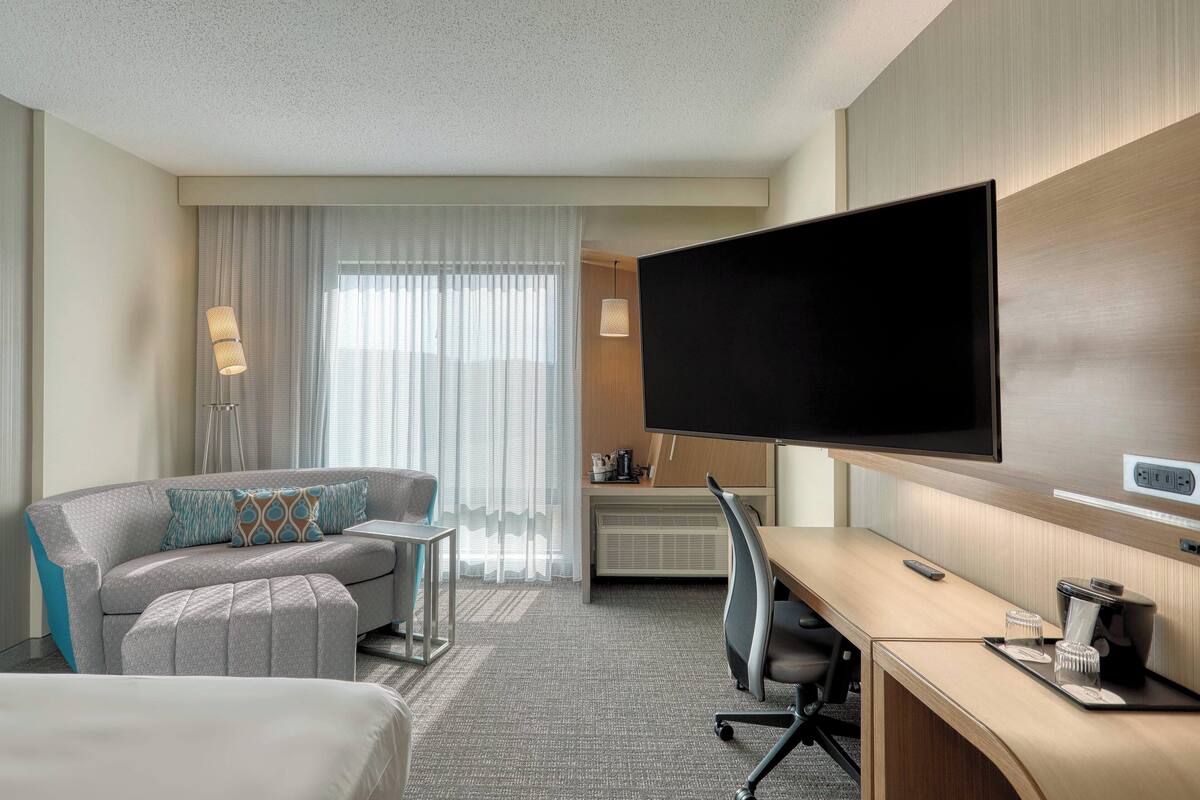 A hotel room with a large flat-screen TV, a sofa, a desk, and a chair.