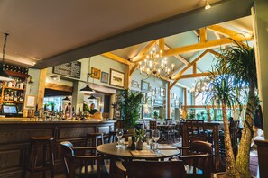 A restaurant with wooden beams, a bar area with bottles, and framed pictures on the walls.