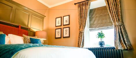 A neatly made bed with a blue and white duvet, a red headboard, and a window with patterned curtains.