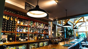 Un bar avec un assortiment de bouteilles d’alcool, une caisse enregistreuse et un espace où sont disposées des tables et des chaises.