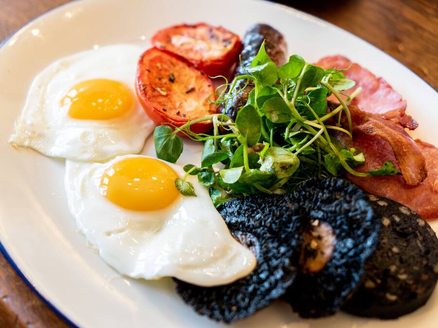 En tallerken med æg, tomater, grønt og bacon.