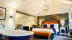 Une chambre avec une grande baignoire, un lit avec une tête de lit orange et un lustre.