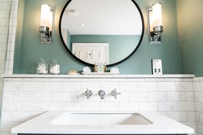 A bathroom with a white sink, a round mirror, and two wall-mounted light fixtures. - Arrow Mill (Alcester)