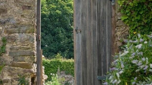 A rustic stone archway leading to a wooden door with a metal latch, surrounded by greenery and a stone base. - Cuffern Manor (Haverfordwest)