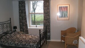 A bedroom with a bed, a chair, a window with curtains, and a framed picture on the wall. - Cuffern Manor (Haverfordwest)