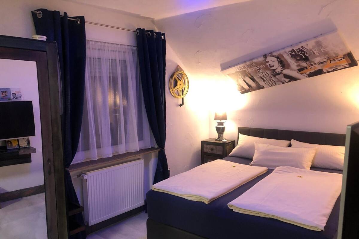 Un dormitorio con dos camas, una ventana con cortinas, un reloj de pared, un cartel y una lámpara de noche.