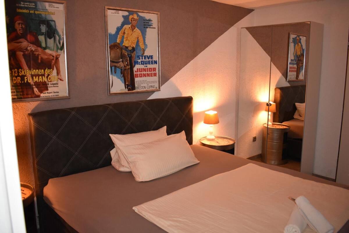 Habitación de hotel con una cama grande, cabecera, mesita de noche con lámpara y un cartel en la pared.