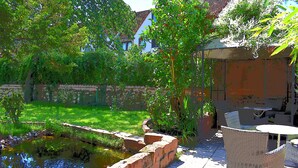 Un patio con un pequeño estanque, mobiliario de mimbre y un muro de ladrillo.