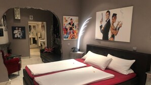 Una habitación de hotel con una cama grande, una pared de acento roja, un cuadro de un hombre con un arma y un reloj en la pared.