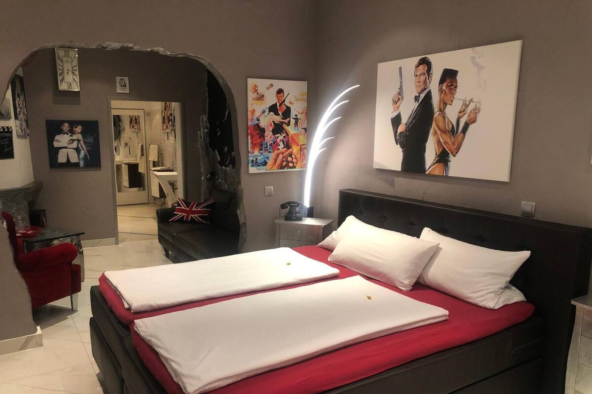Una habitación de hotel con una cama grande, una pared de acento roja, un cuadro de un hombre con un arma y un reloj en la pared.