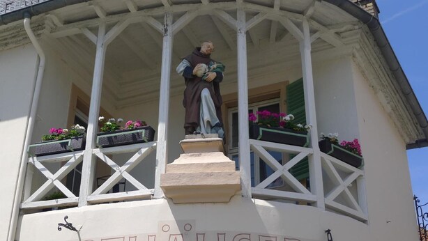 Un edificio con balcón, estatua y macetas con flores.