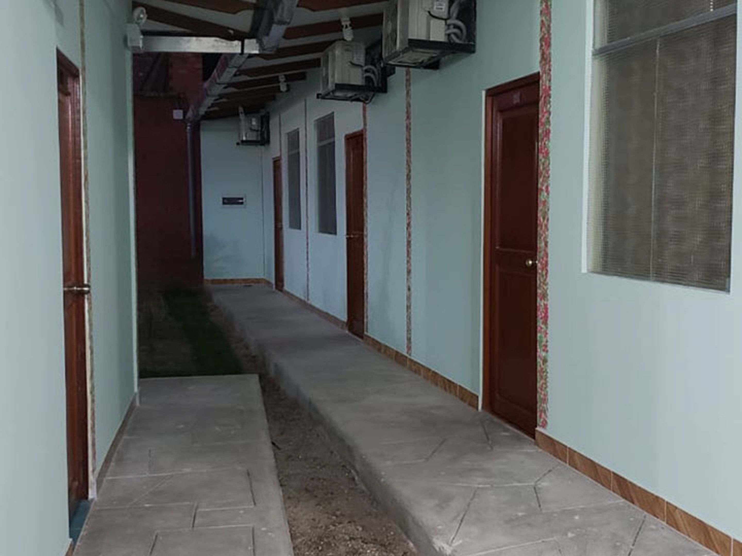 Un pasillo con puertas a ambos lados, suelo de baldosas y unidades de aire acondicionado en el techo.