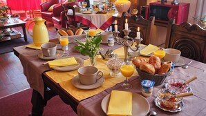 A breakfast table set with various breakfast items, including croissants, orange juice, and a candle holder. - Les Roses (Santec)