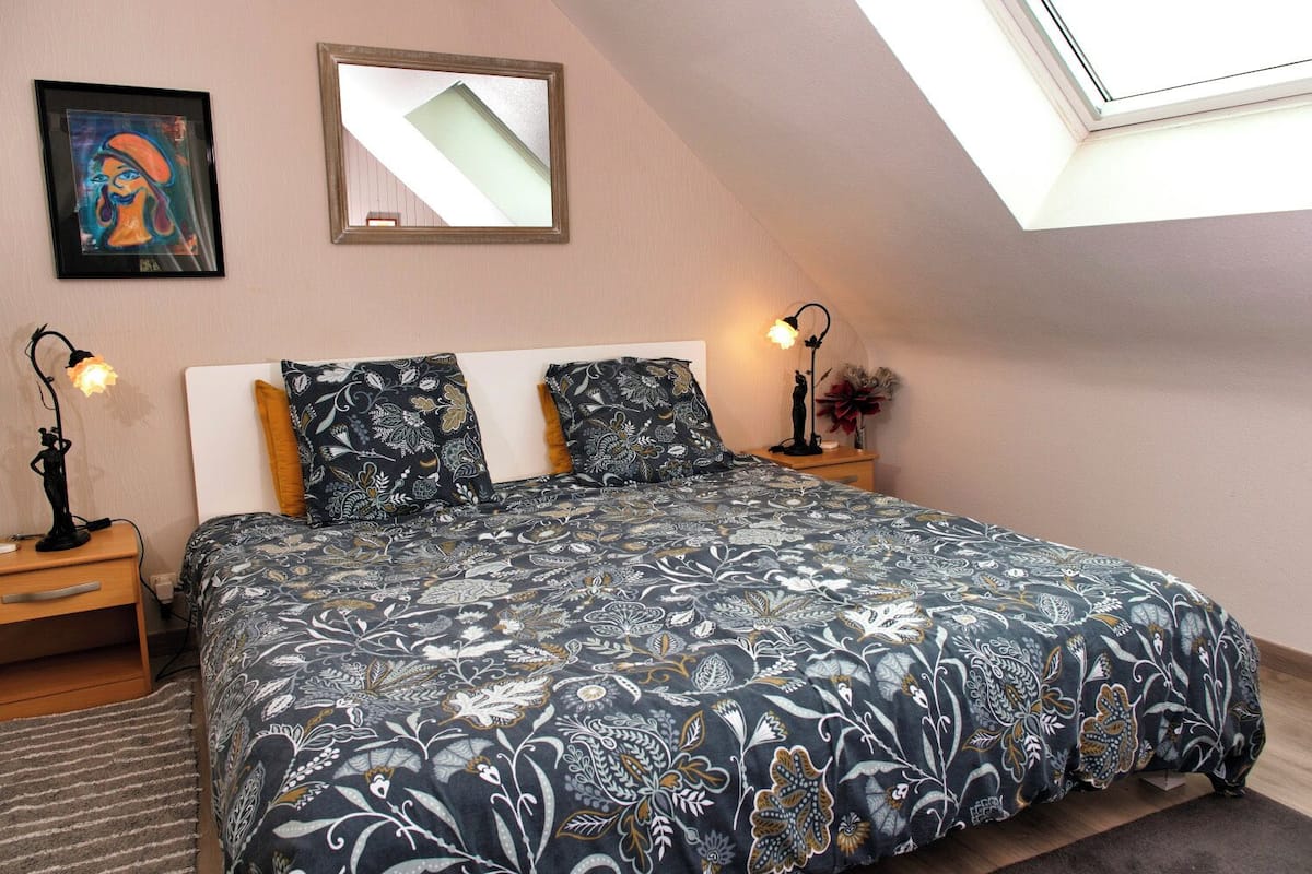 A bedroom with a large bed, two bedside lamps, a framed picture, and a skylight.