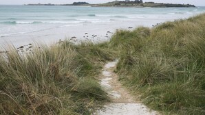 A coastal path leading to a beach with a distant view of a hill with buildings. - Les Roses (Santec)