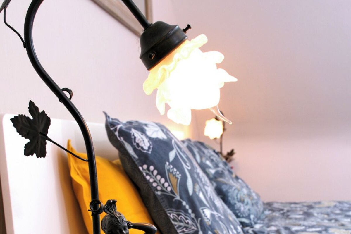 Un lit avec une literie à motifs, une lampe de sol noire ornée d’une figurine décorative et un coussin jaune.