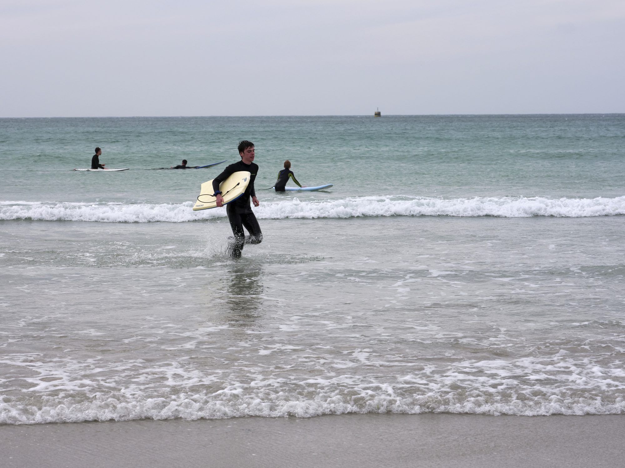 Rantakuva, jossa surffaaja kävelee kohti vettä, mukanaan surffilauta.