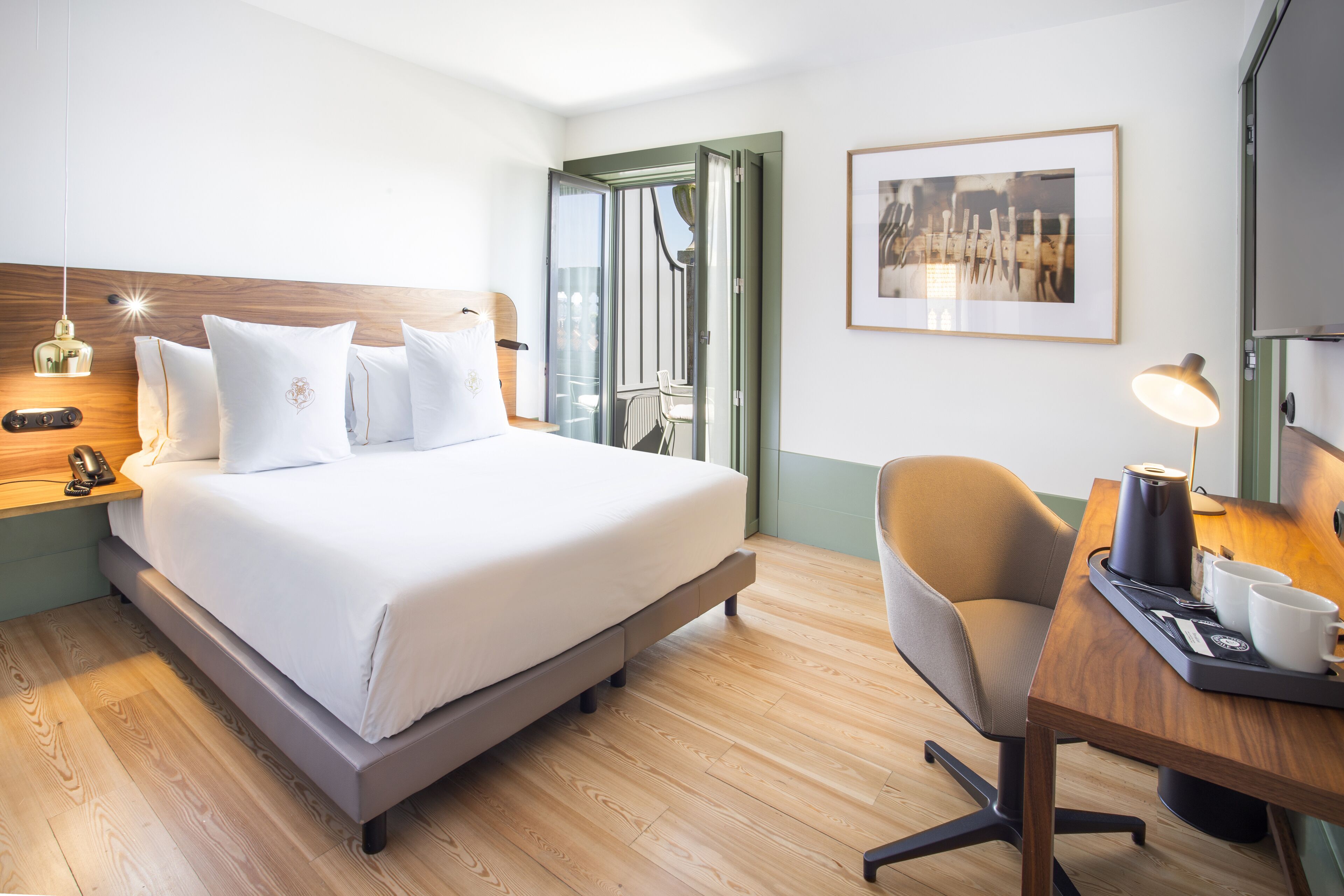 Habitación de hotel moderna con una cama grande, un escritorio con una silla, una cafetera y un cuadro en la pared.
