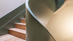 A spiral staircase with wooden steps and a green handrail. - One Shot Aliados Goldsmith  (Porto)