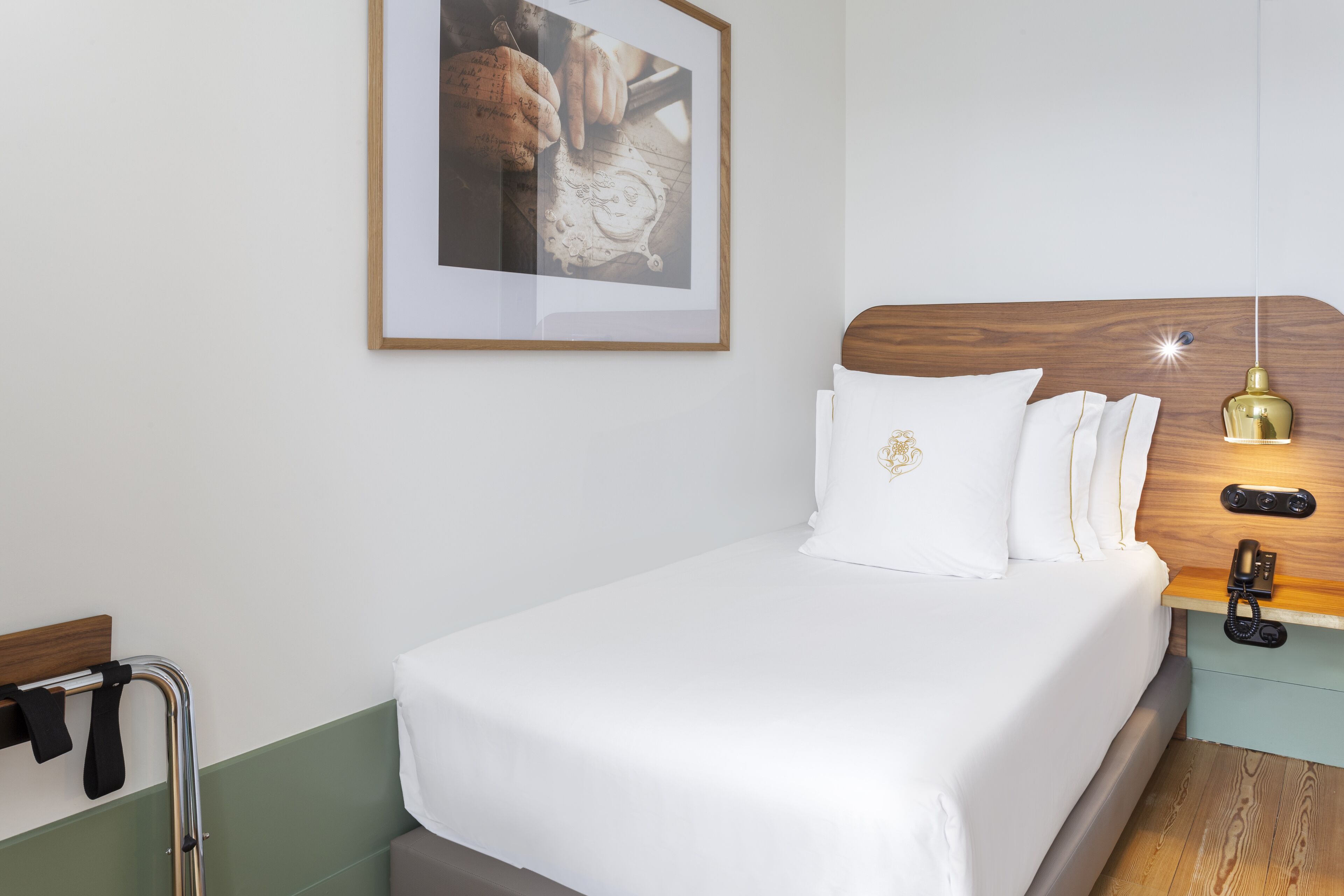 A neatly made bed with white linens, a wooden headboard, a bedside table with a lamp, and a framed picture on the wall.