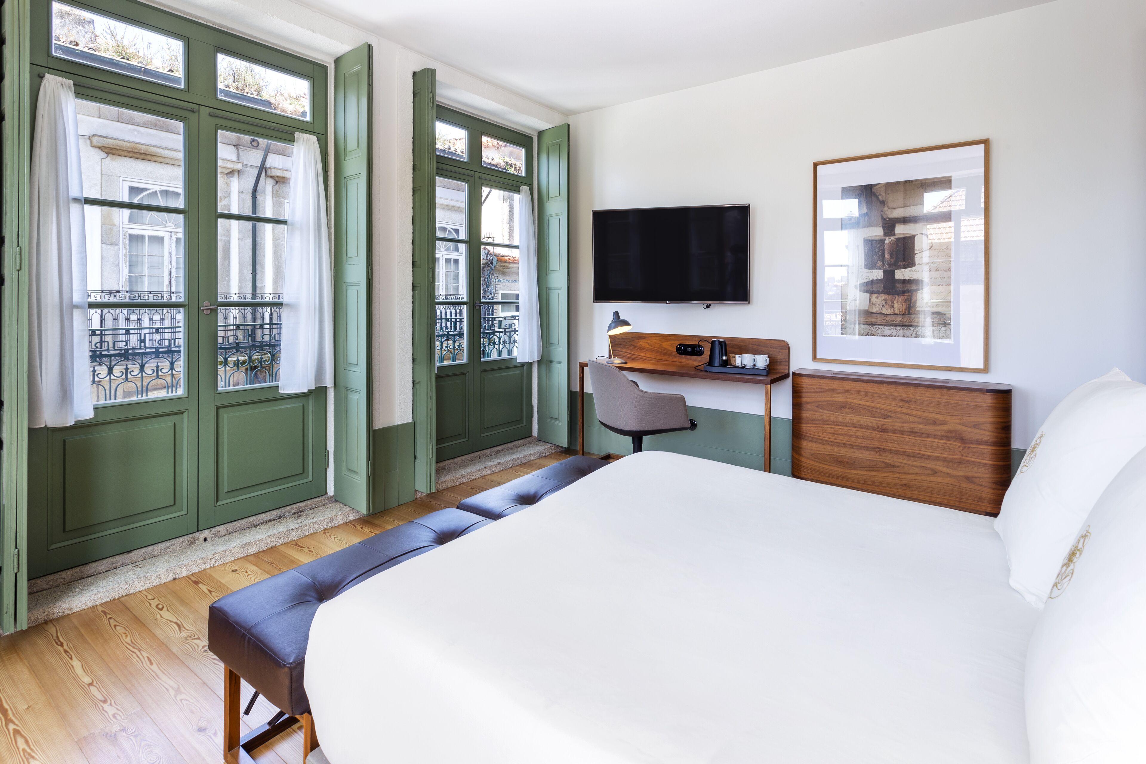 A hotel room with a large bed, a desk with a chair, a television, and a framed picture on the wall.