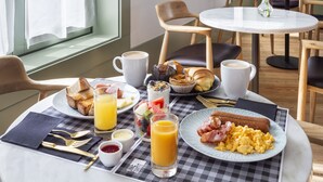 A breakfast table with croissants, toast, scrambled eggs, bacon, sausages, and orange juice. - One Shot Aliados Goldsmith  (Porto)