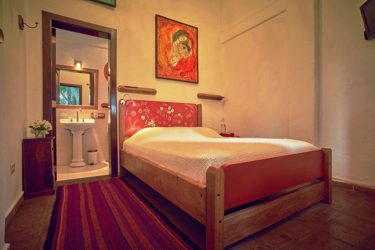 Een slaapkamer met een houten bed, een rood hoofdeinde, een wit wastafelmeubel en een spiegel.