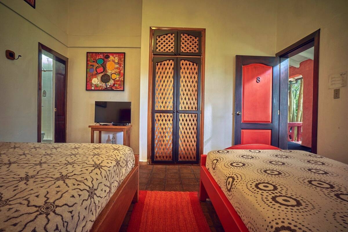 Een hotelkamer met twee bedden, een televisie op een bijzettafeltje, een decoratieve deur en een schilderij aan de muur.