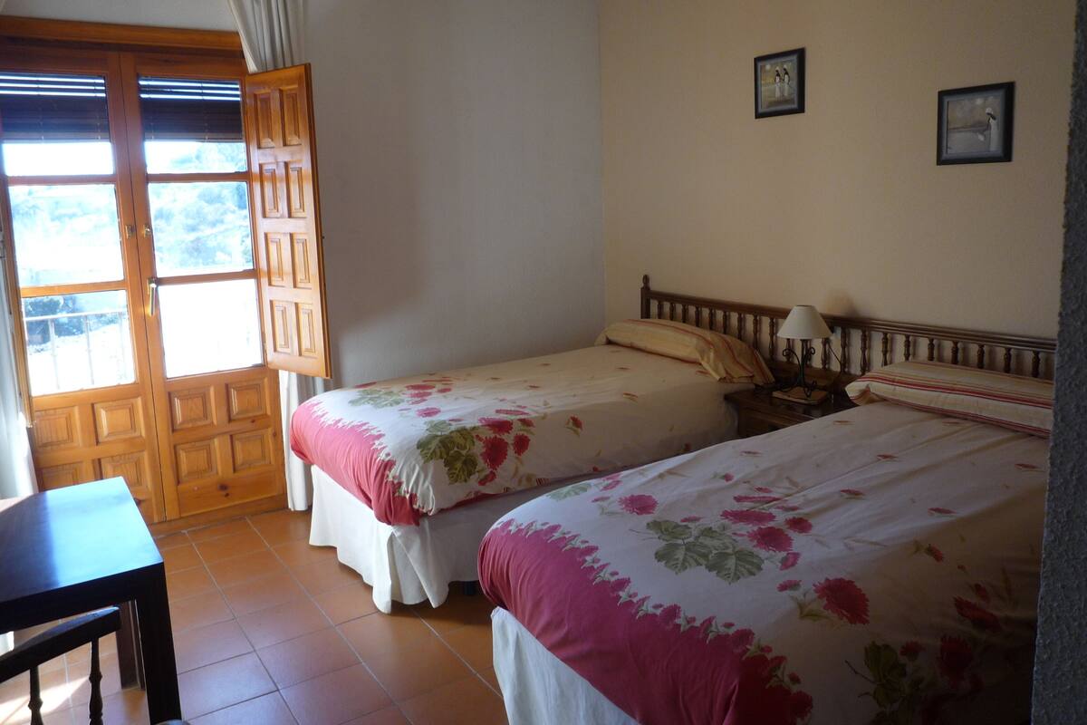 A bedroom with two beds, a wooden door, a small table, and a nightstand with a lamp.