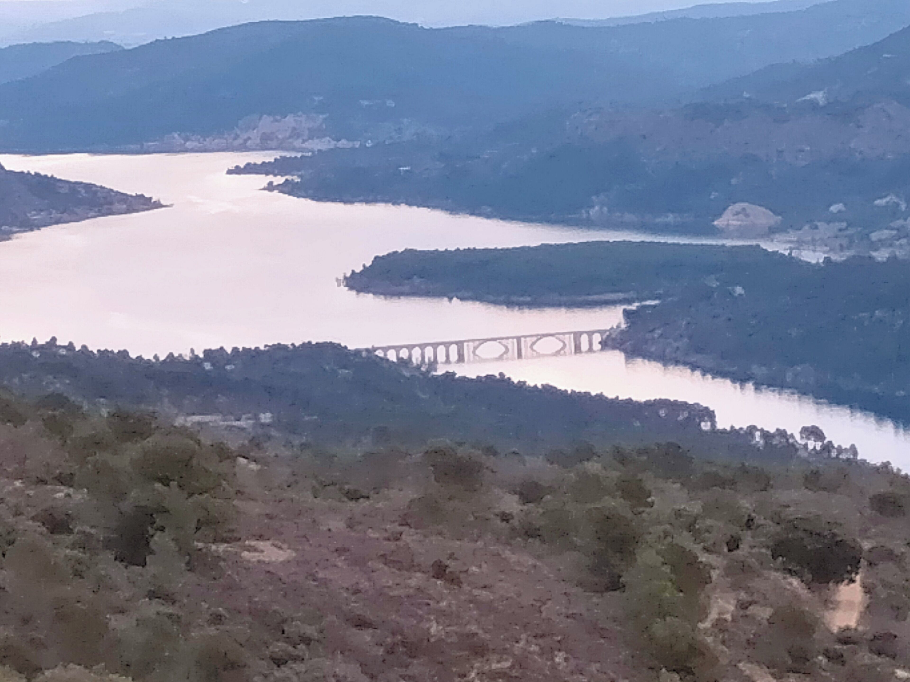 Un río con un puente, rodeado de colinas y vegetación escasa.