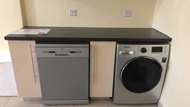 A compact kitchen with a dishwasher and a front-loading washing machine. - Isaac Anthony Homes (Accra)