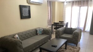 A living room with a sofa, armchairs, a coffee table, and a dining table. - Isaac Anthony Homes (Accra)