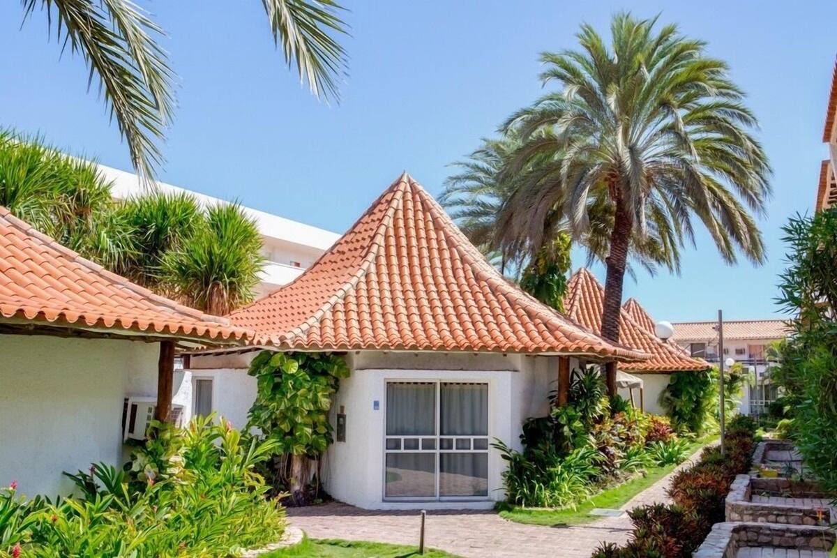 A row of villas with red-tiled roofs, surrounded by lush greenery and palm trees.