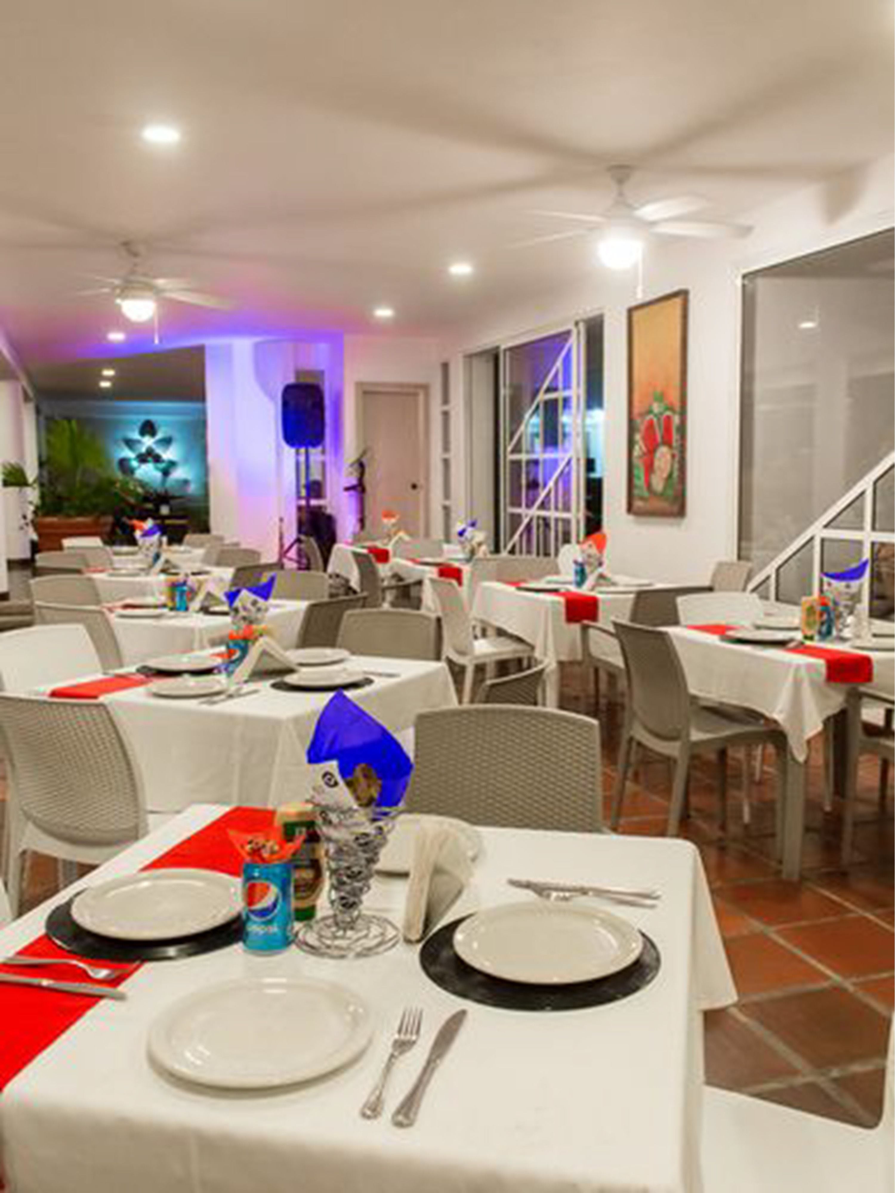 Un restaurant avec de nombreuses tables dressées pour le service, avec des nappes blanches et des serviettes rouges.