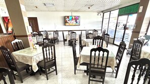 A restaurant with round tables and chairs, a television mounted on the wall, and a view of the street outside. - Hotel Madrid Chiriqui (David)