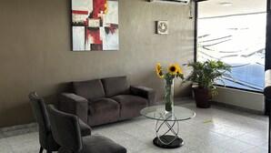 A modern waiting area with a sofa, chairs, a glass table with a vase of sunflowers, and a large window offering a view. - Hotel Madrid Chiriqui (David)