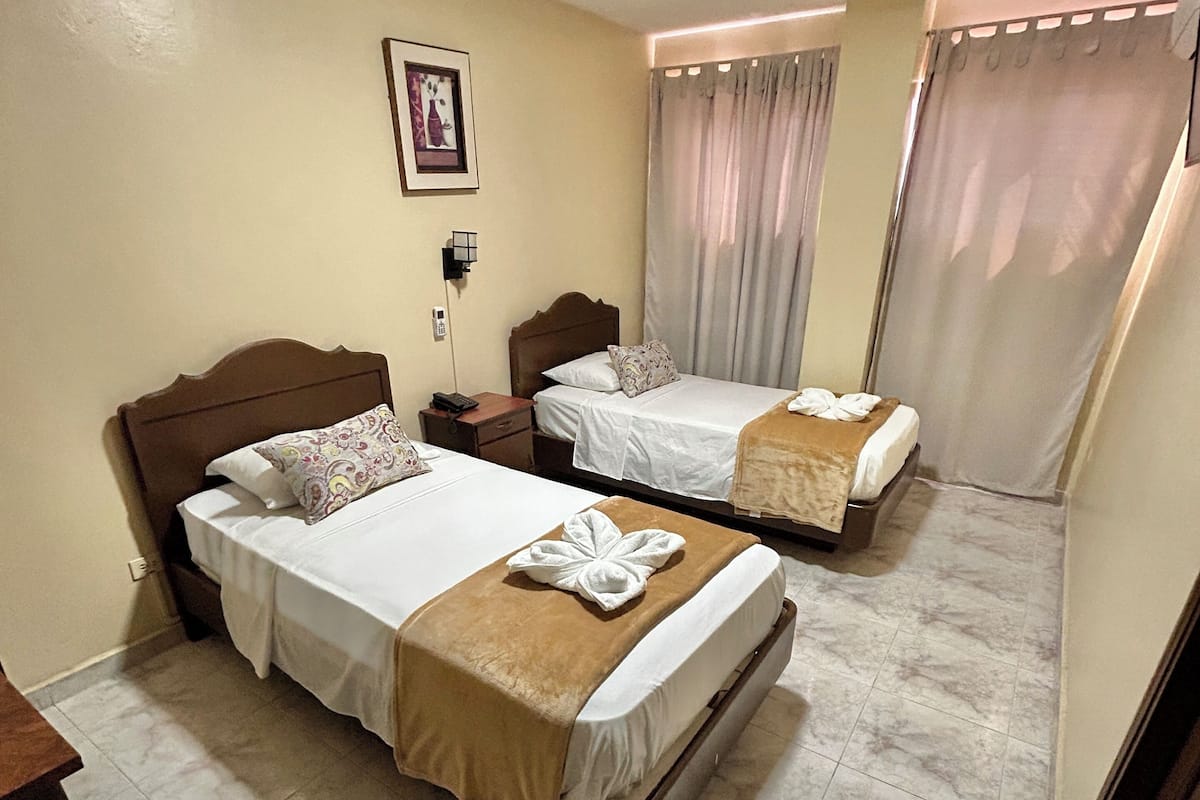 A hotel room with two beds, a nightstand, a wall-mounted phone, and a window with curtains.